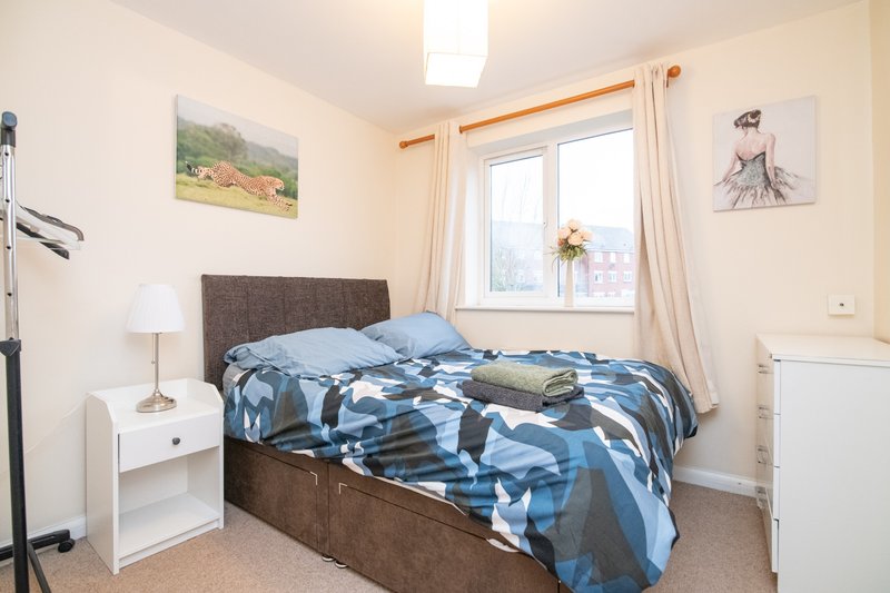 Bedroom with double bed, blue patterned bedding, bedside table, lamp and window
