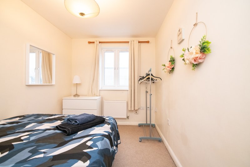 Bright bedroom with double bed, mirrored wardrobe, desk lamp, hanging floral decor and window with curtains