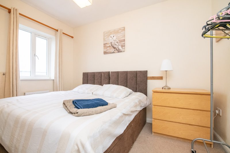 Bright bedroom with double bed, wooden dresser, bedside lamp and window with curtains