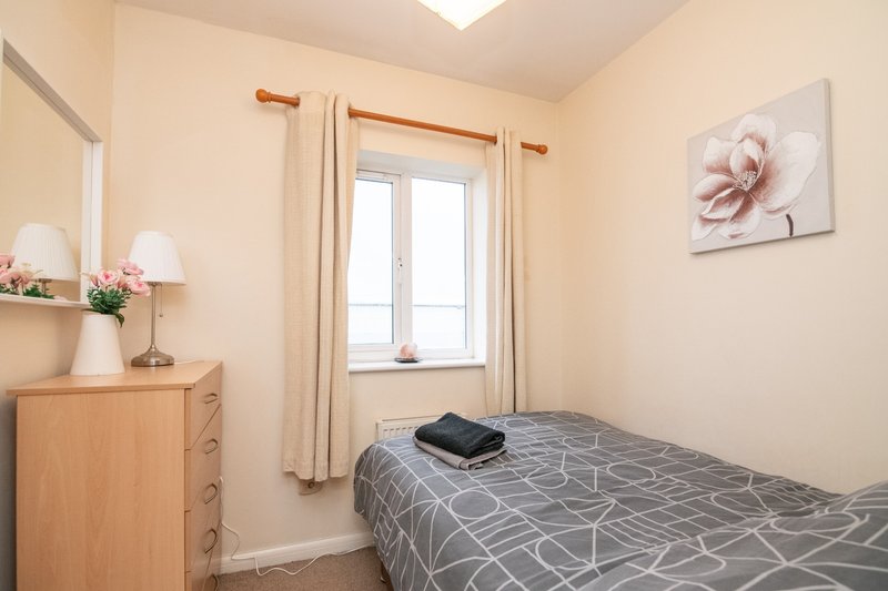 Small bedroom with single bed, wooden dresser, window with curtains and pink floral wall art