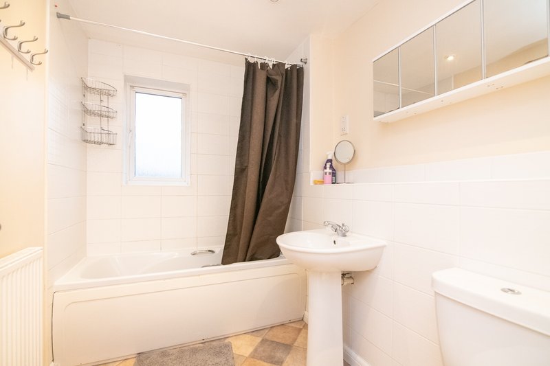 Clean bathroom with bathtub, brown shower curtain, pedestal sink and toilet