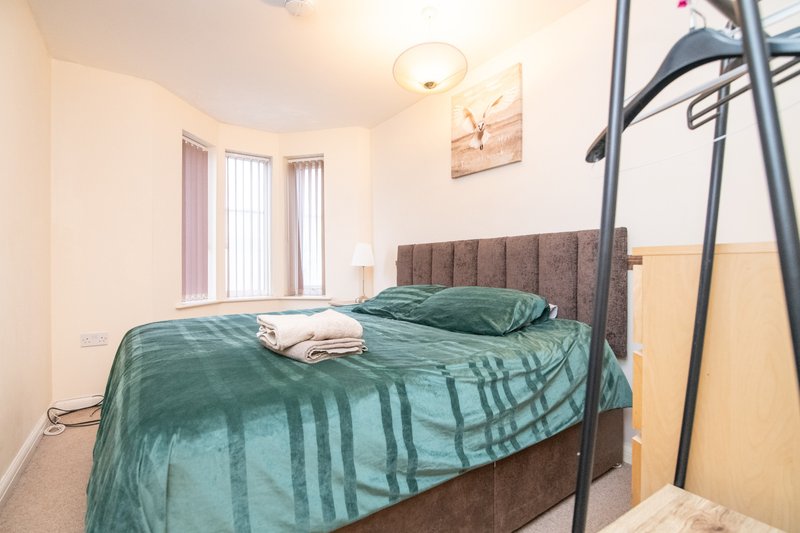 Bedroom with double bed, green bedding, upholstered headboard, and vertical blinds