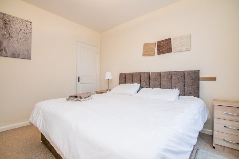 Bright bedroom with double bed, grey upholstered headboard, bedside lamp and wooden nightstand