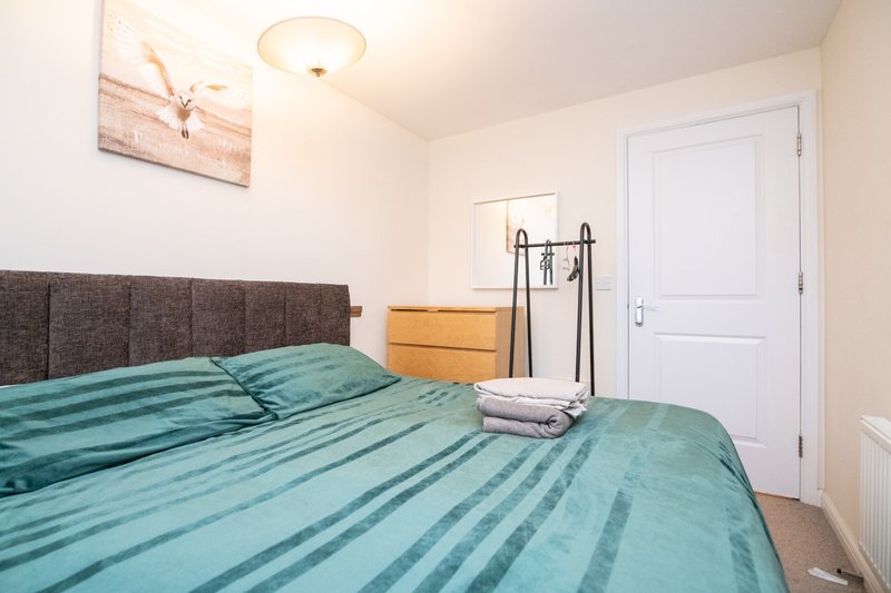Bedroom with double bed, teal bedding, grey headboard, wooden dresser and white door