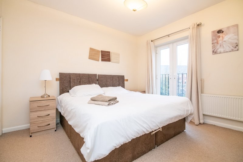 Bright bedroom with double bed, wooden bedside table, lamp, and balcony doors