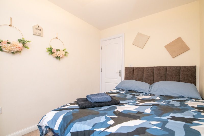 Bedroom with double bed, upholstered headboard, blue patterned bedding and wall-mounted floral decor