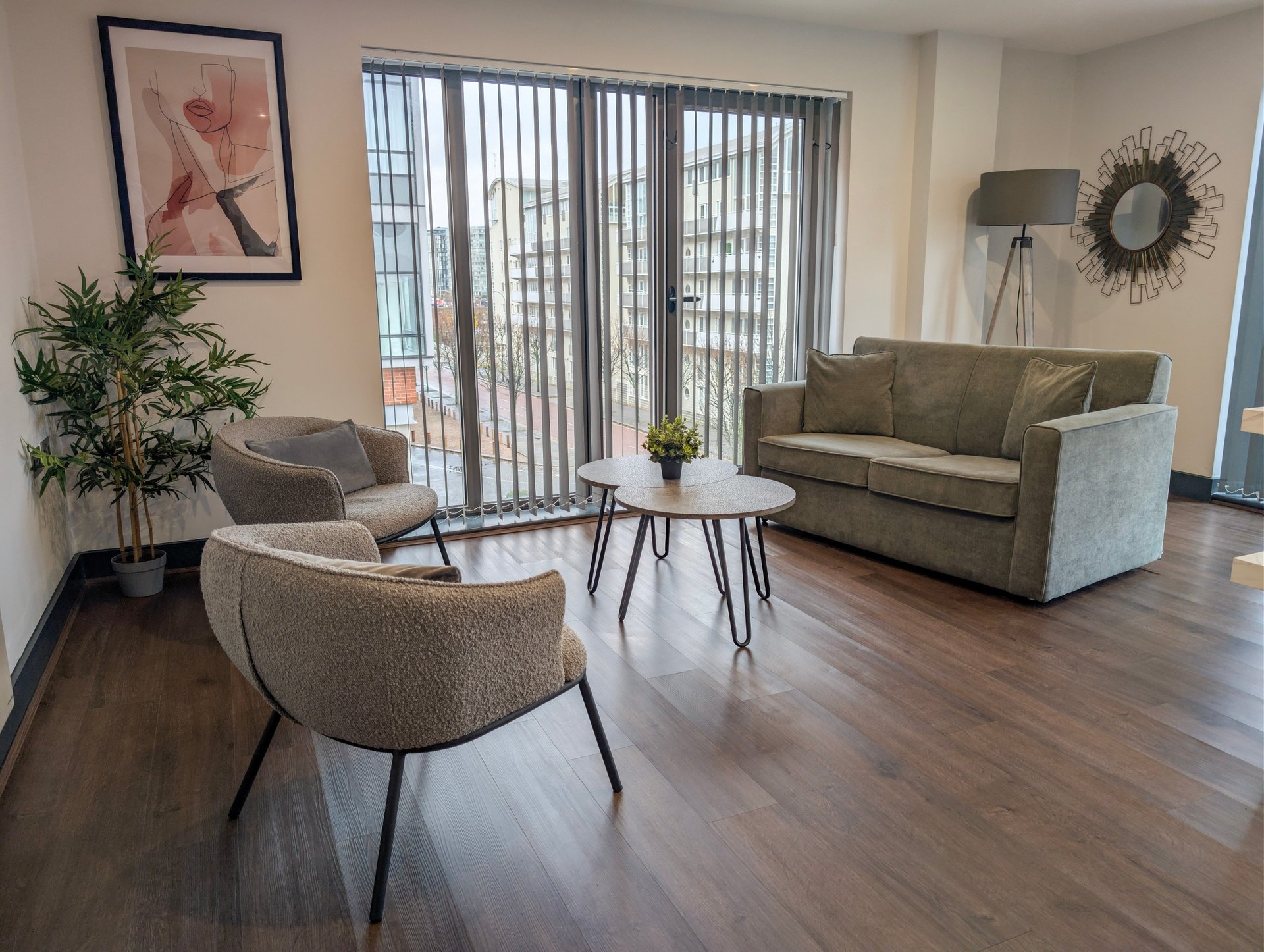 Modern living room with gray upholstered furniture, wooden floors, and large windows with vertical blinds