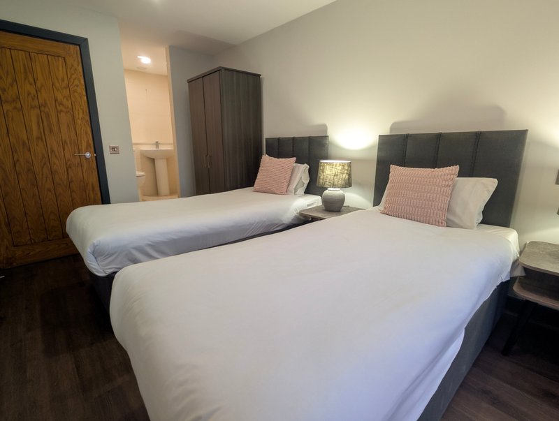 Modern twin bedroom with two beds, pink cushions, bedside lamps and ensuite bathroom