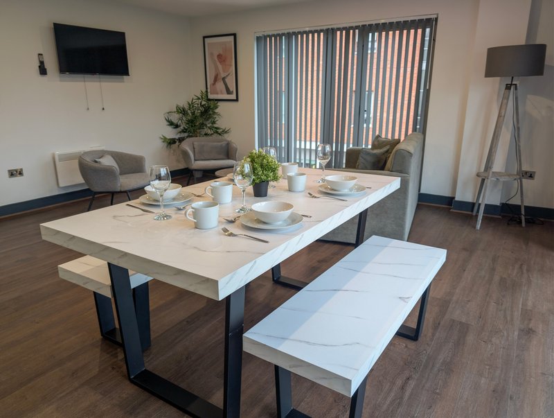 Open-plan living and dining space with marble table, seating area, TV, and vertical blinds