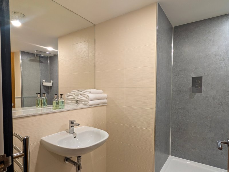 Modern bathroom with white sink, large mirror, stacked towels and walk-in shower