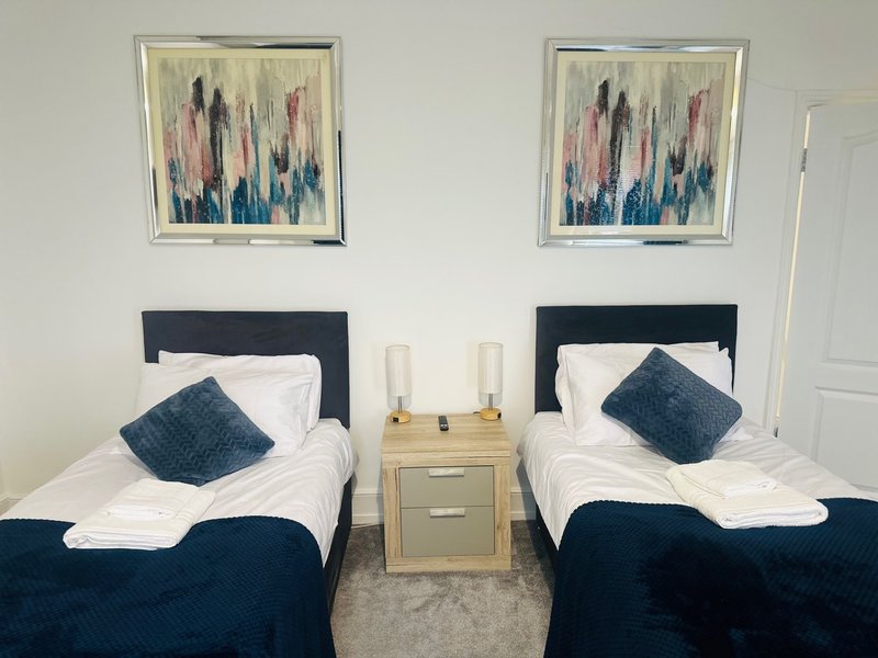 Twin bedroom with two single beds, dark headboards, white bedding, navy cushions and shared nightstand
