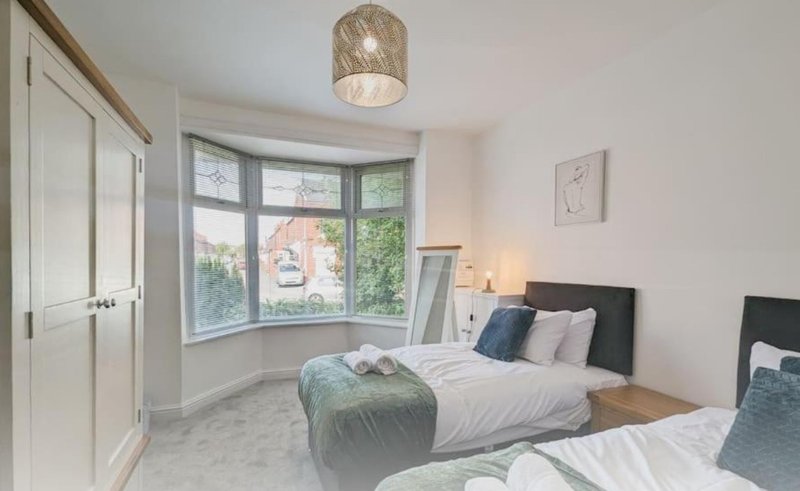Bright bedroom with two beds, bay window, wardrobe, and pendant light fixture
