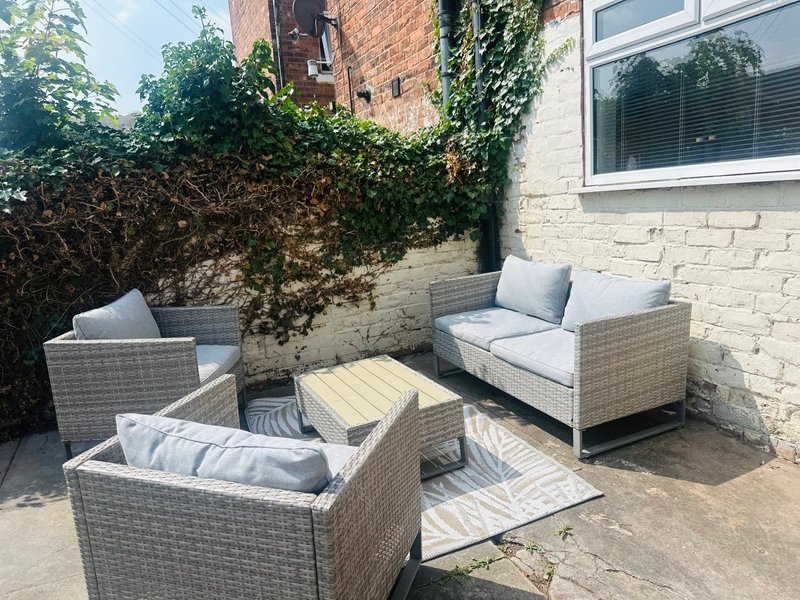 Outdoor patio with rattan furniture, cushions, wooden table and ivy-covered walls