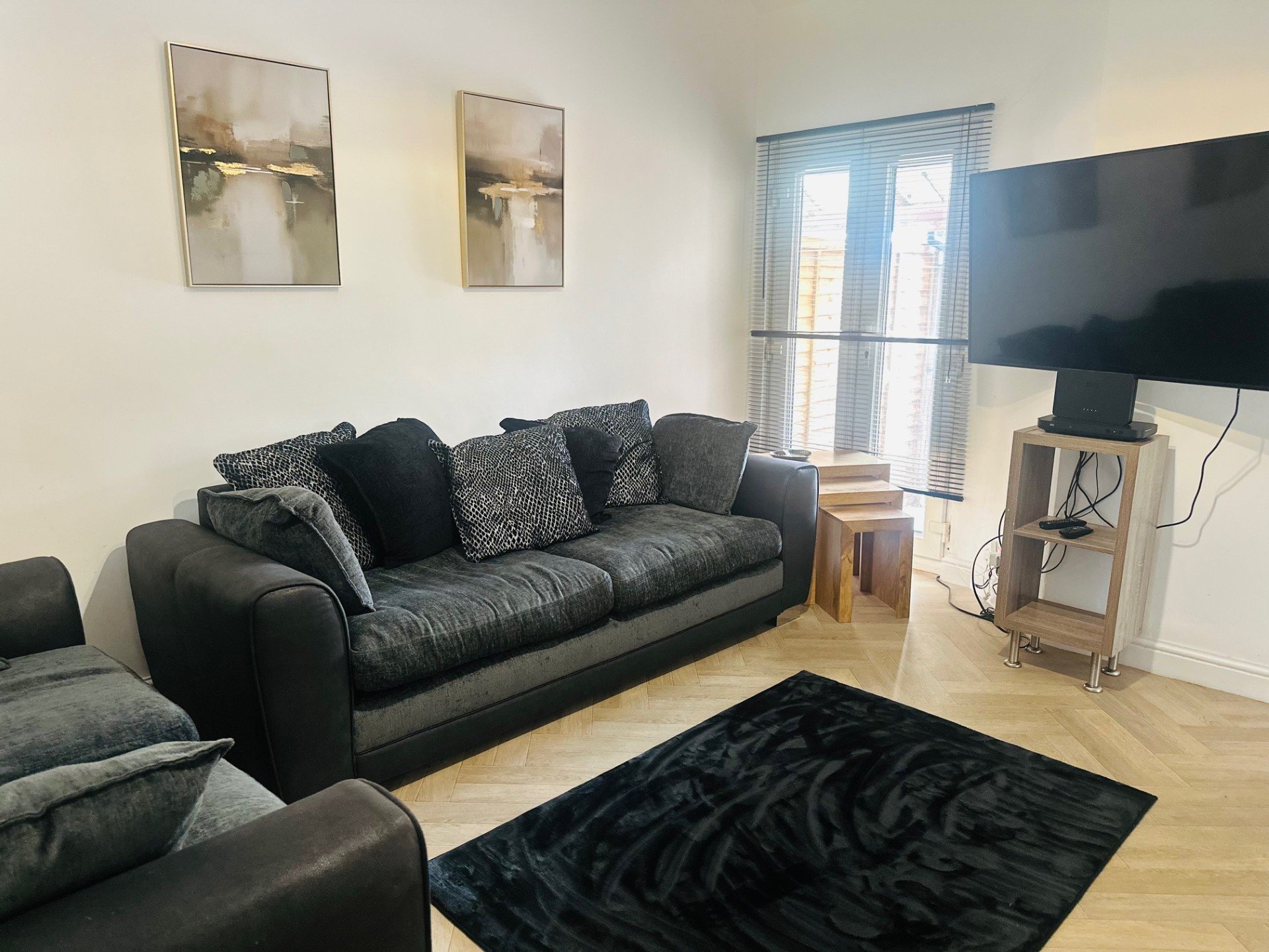 Living room with black leather sofa, patterned cushions, TV on stand, and wooden flooring
