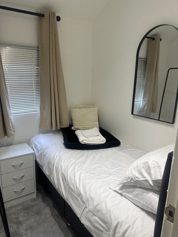 Compact bedroom with single bed, white bedding, black metal frame and mirror