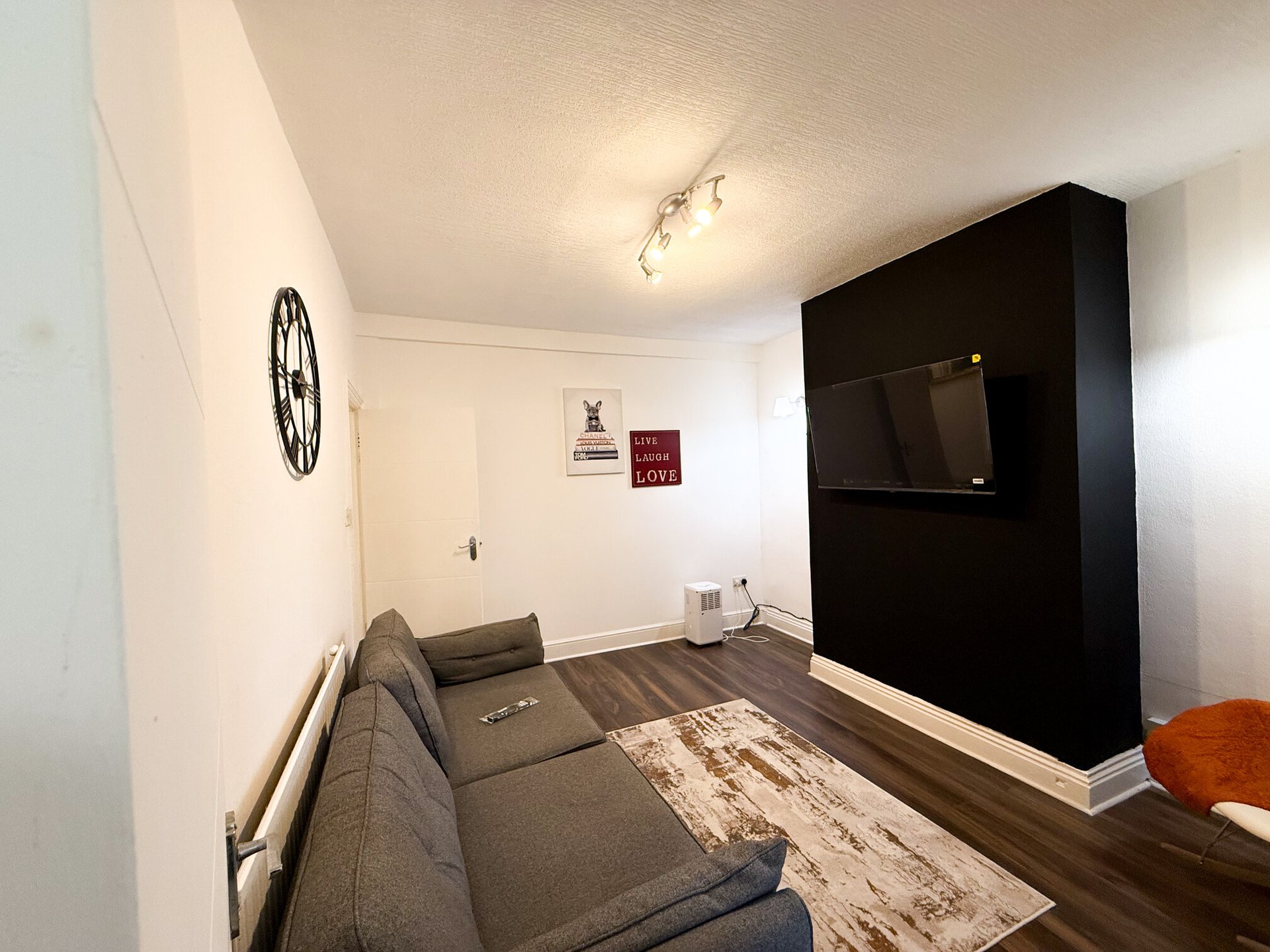 Living room with grey sofa, black TV unit, wooden floor and wall clock