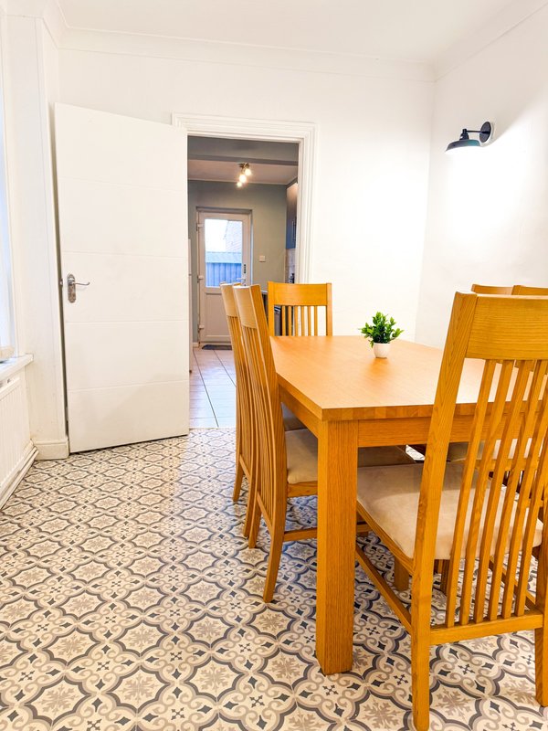 Dining area with wooden table, chairs, and patterned tile floor leading to hallway