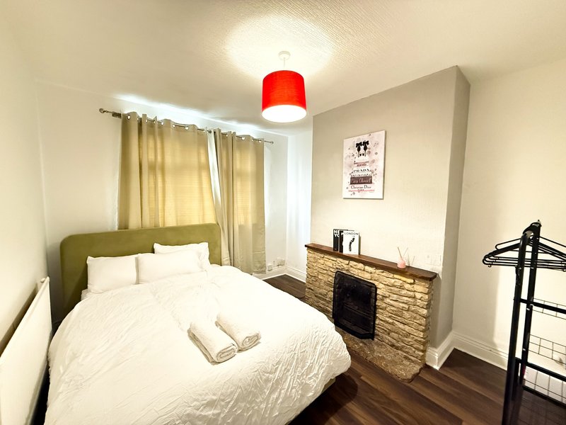 Bedroom with double bed, olive headboard, white bedding, wooden dresser and red ceiling lamp