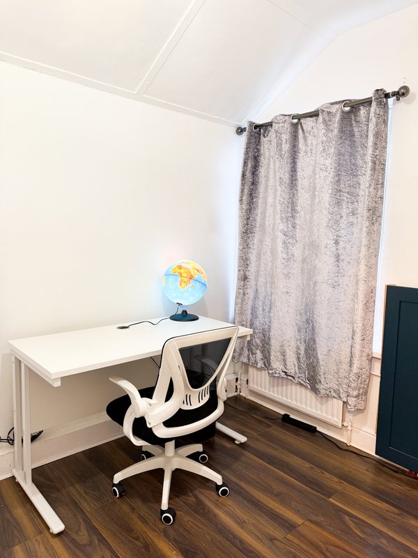 Home office with white desk, ergonomic chair, globe lamp, and grey curtains