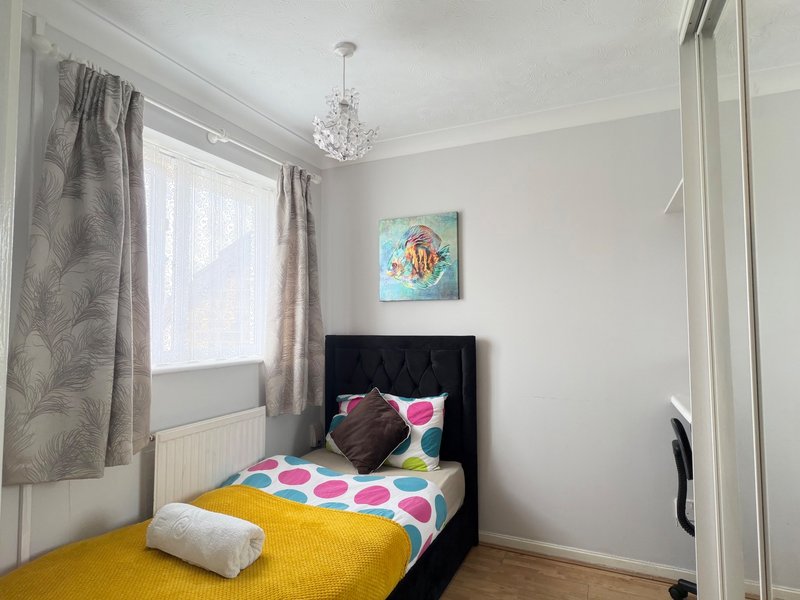 Bright bedroom with black bed, colorful bedding, window with grey curtains and crystal pendant light