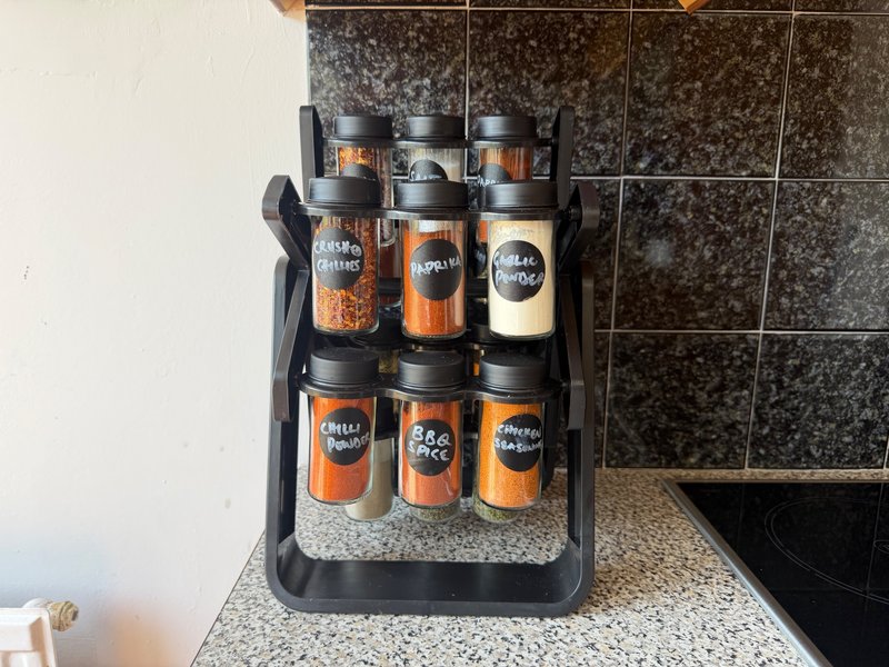 Kitchen counter with spice rack containing labeled jars and dark tile backsplash