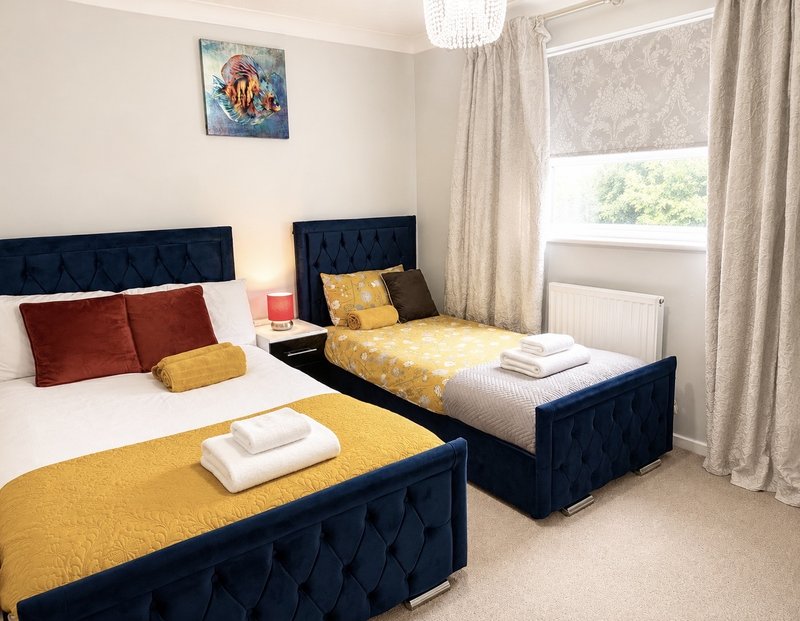 Bright bedroom with two single beds, navy headboards, yellow bedding, cushions and window with curtains