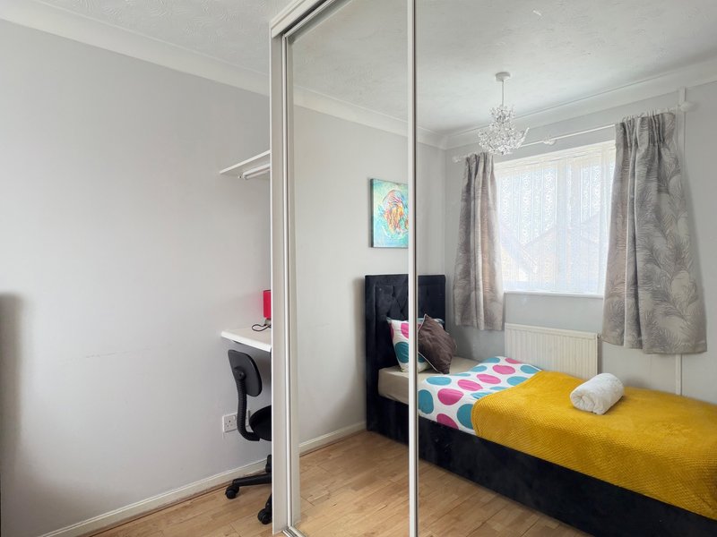 Bedroom with double bed, yellow bedding, mirrored wardrobe, desk chair and window with grey curtains