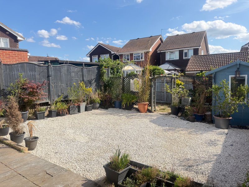 Suburban garden with gravel patio, potted plants, wooden fences and brick houses