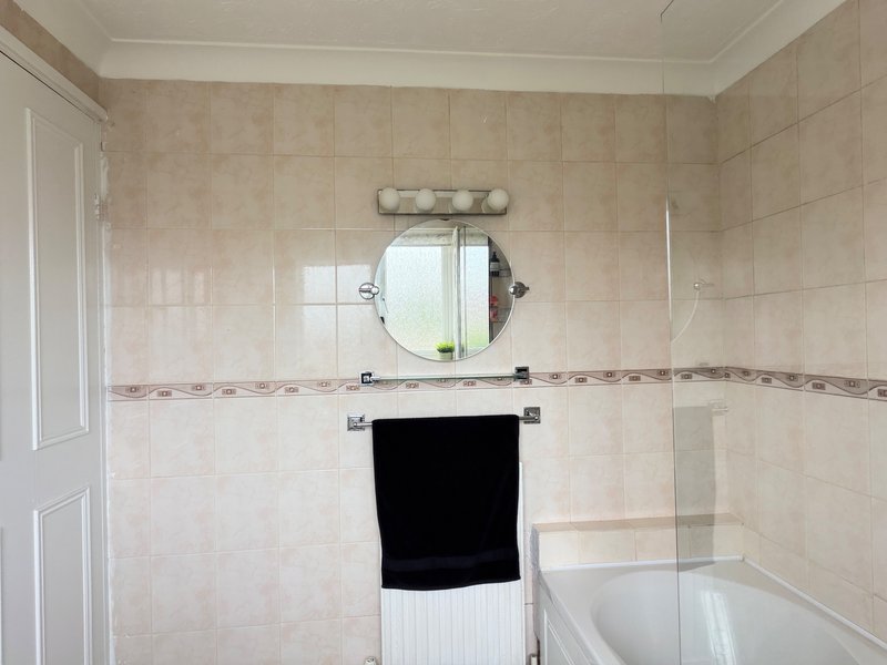 Bathroom with beige tile walls, round mirror, sink vanity and bathtub with glass screen