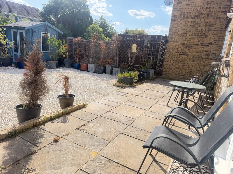 Paved garden courtyard with seating, potted plants, fencing and brick buildings