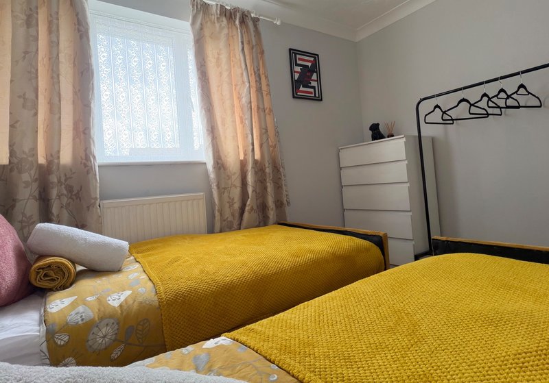 Bright bedroom with two single beds with yellow bedding, window with beige curtains, white dresser