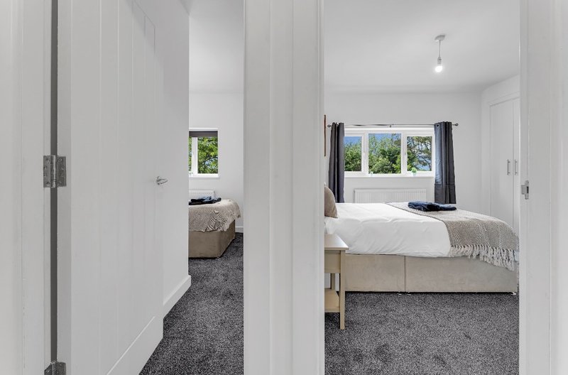 Modern bedroom with double bed, grey carpet, white walls and large window with garden view