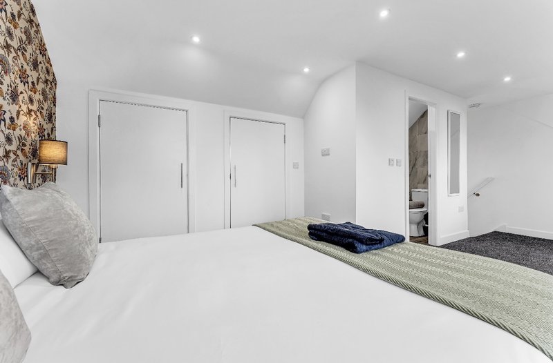 Modern bedroom with white bed, exposed stone wall, built-in wardrobes and ensuite door