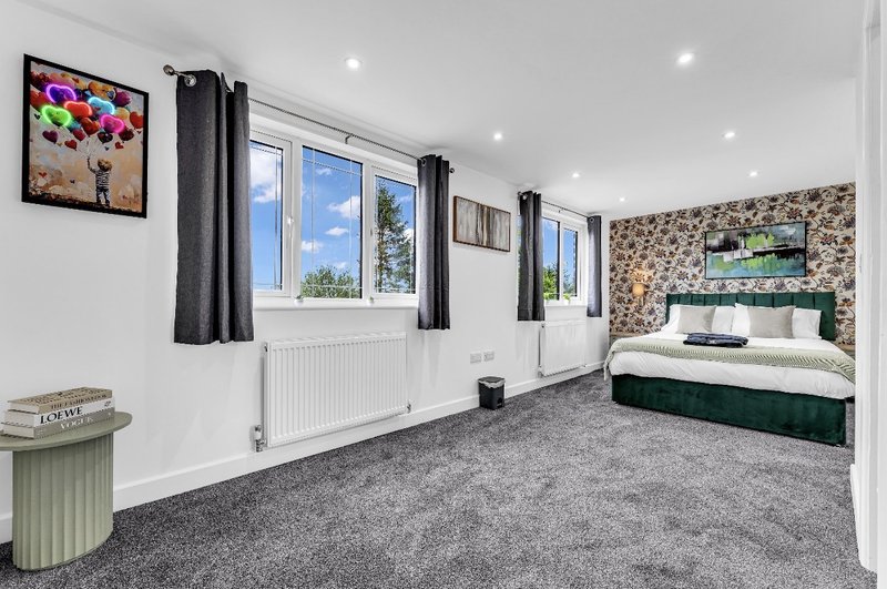 Spacious bedroom with double bed, multiple windows, grey carpet and framed artwork on walls