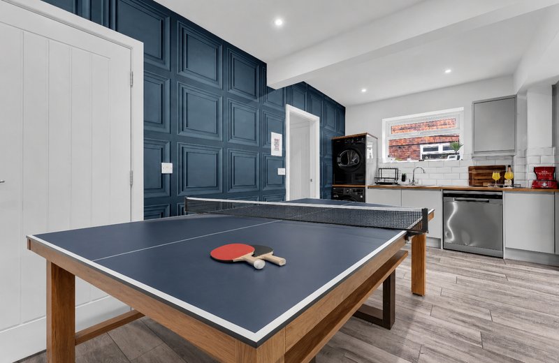 Games room with ping-pong table, dark blue paneling, kitchen area and white cabinetry