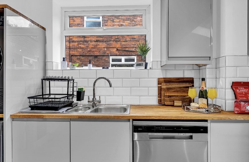 Modern kitchen with white cabinetry, wooden countertop, stainless steel sink and appliances