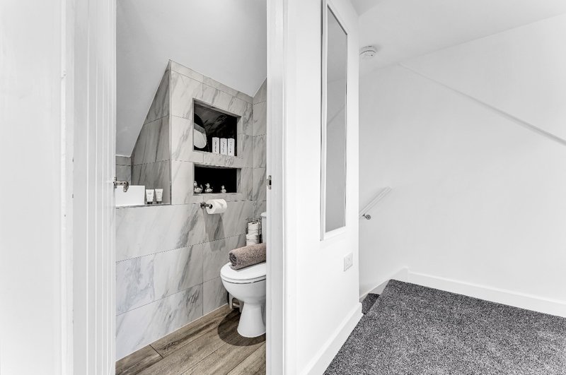 Modern bathroom with marble-tiled walls, white toilet, recessed shelving and wooden floor