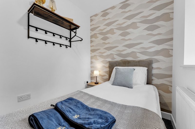 Compact bedroom with single bed, geometric headboard, wall shelf and bedside lamp