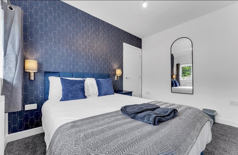 Modern bedroom with blue patterned feature wall, white bed, wall sconces, and arched mirror