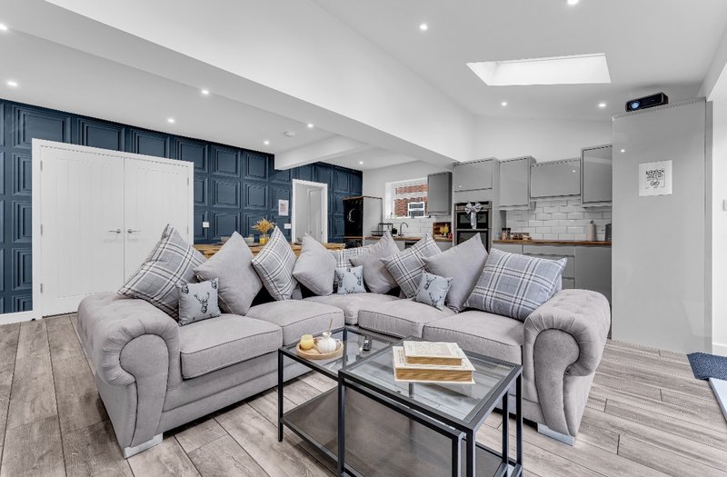 Open-plan living area with grey corner sofa, coffee table, and kitchen with blue cabinetry