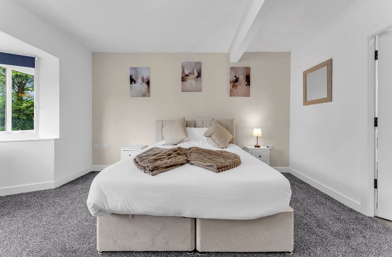 Bright bedroom with double bed, neutral bedding, fur throw, and framed wall art