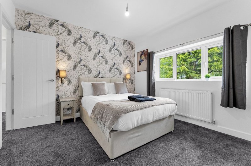 Bright bedroom with double bed, patterned headwall, wooden nightstands and large windows