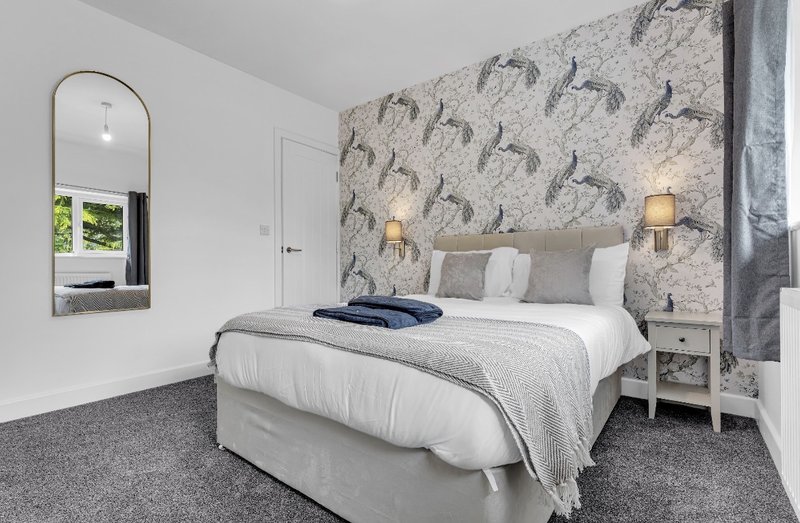 Modern bedroom with double bed, patterned headboard wall, mirror, and grey carpet flooring