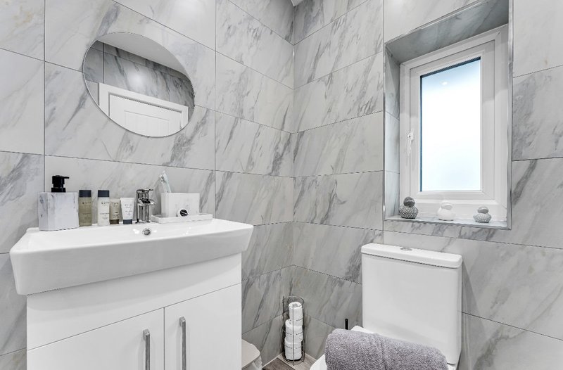 Modern bathroom with marble tiles, white vanity, mirror, toilet and towels