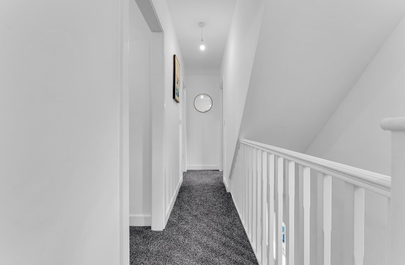 Clean white hallway with gray carpet, white railing, and ceiling light fixture