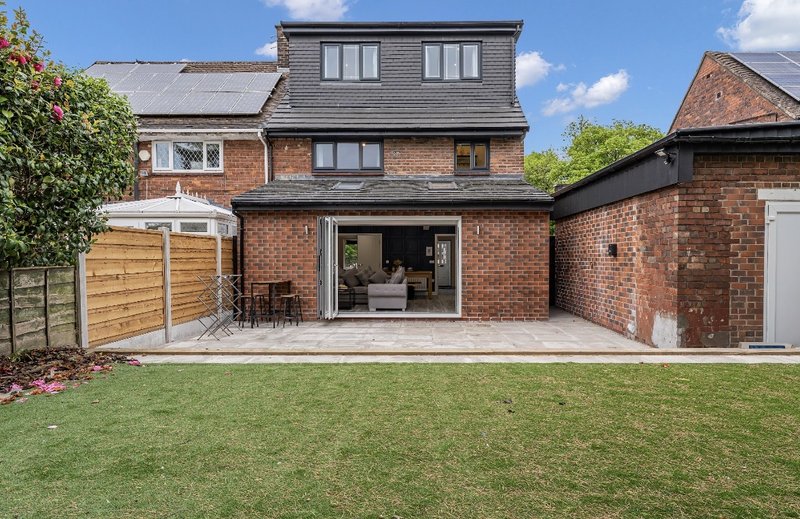 Brick house with patio extension, manicured lawn, wooden fence and garden views