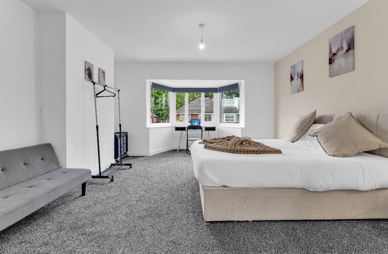Spacious bedroom with double bed, grey carpet, small sofa and bay window