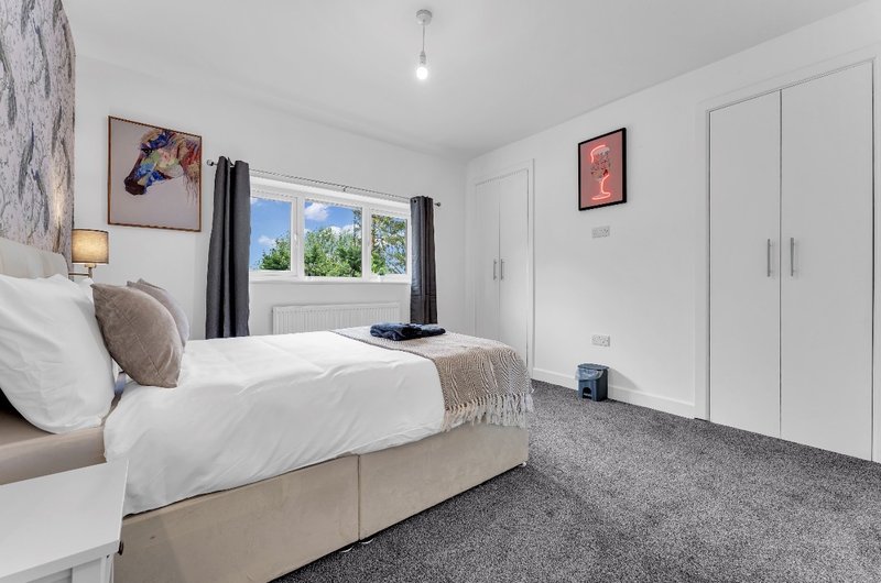 Modern bedroom with double bed, grey carpet, white wardrobes and window with garden view