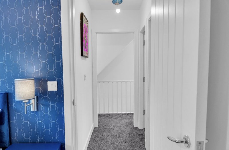 Bright hallway with blue patterned wallpaper, white doors, and gray carpet flooring