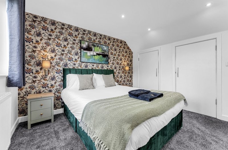 Modern bedroom with double bed, patterned accent wall, bedside table and white fitted wardrobes